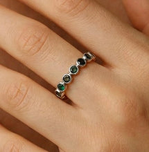 Load image into Gallery viewer, Hand wearing a ring with green gemstones on a neutral background