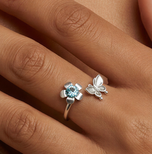 Load image into Gallery viewer, Hand wearing a ring with a blue gemstone and silver butterfly design on beige fabric.